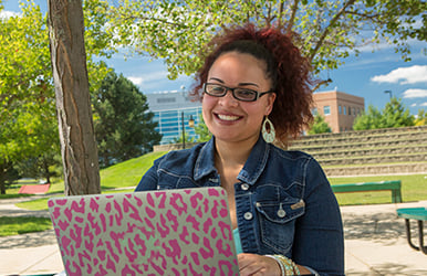 Student with laptop posing in front of campus